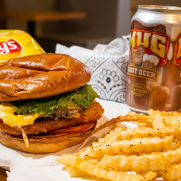 A fried chicken sandwich with fries, a bag of chips, and a can of Mug Root Beer.