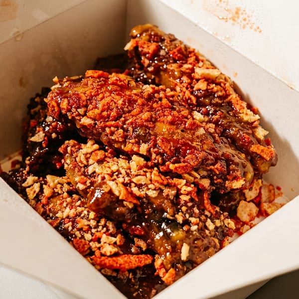 Crispy, glazed chicken wings topped with red and tan crunchy bits in a white takeout box.