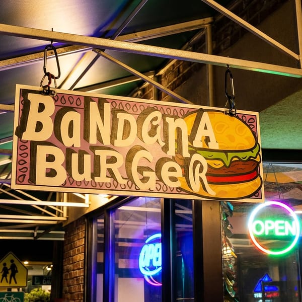 A colorful "BaNdAnA BuRgEr" sign with a burger graphic hangs above an "OPEN" neon sign.