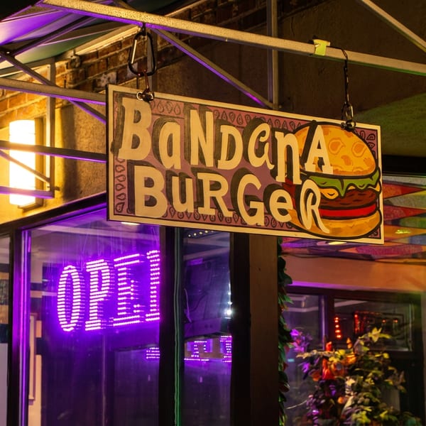 Bandana Burger restaurant sign with a neon "OPEN" sign and colorful string lights in the window at night.